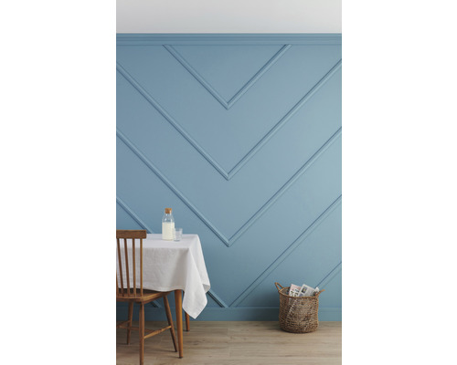 Innenraum mit blau gestrichener Wand mit Zierleisten, Tisch mit weißer Decke, Stuhl und Korb