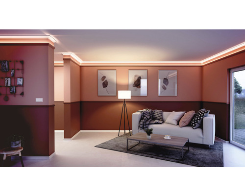 Wohnzimmer mit Stuckprofilen und indirekter Beleuchtung an der Decke, ergänzt durch eine Couch und Dekoration