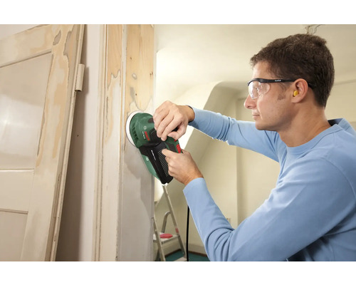 Ein Mann schleift mit einem Exzenterschleifer einen Türrahmen.