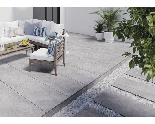 Terrasse mit grauen Fliesen, Gartenmöbeln und Pflanzen.