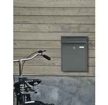 Grauer Briefkasten an einer Holzwand mit einem Fahrrad im Vordergrund