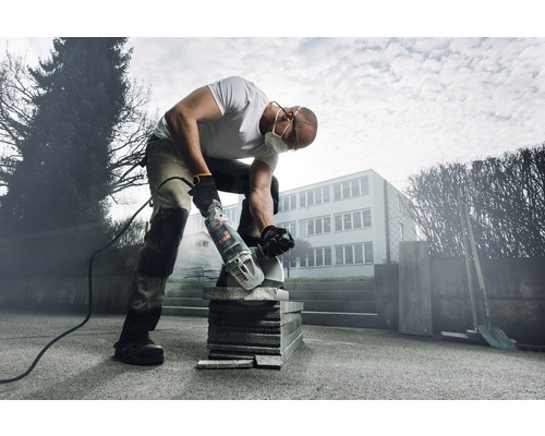 Ein Mann mit Schutzmaske schneidet mit einem Winkelschleifer Pflastersteine