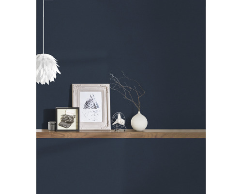 Dekorative Gegenstände wie Bilderrahmen, ein Ventilator und eine Vase auf einem Wandregal vor einer dunklen Wand.