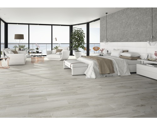 Helles Wohnzimmer mit Bodenfliesen in Holzoptik, Sofa, Sessel und Bett.