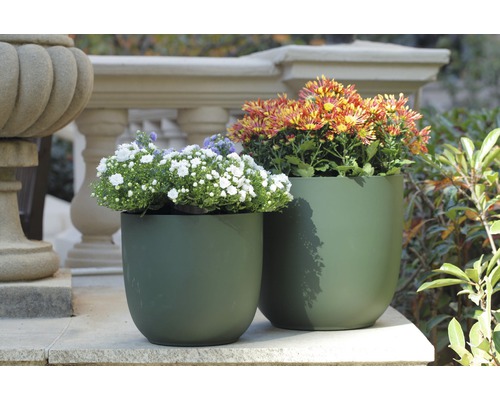Zwei grüne Pflanzgefäße mit Blumen auf einer Steinterrasse
