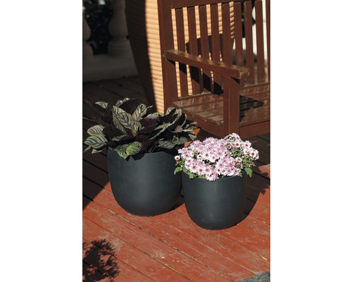 Zwei schwarze Pflanzgefäße mit Pflanzen auf einer Holzterrasse vor einer Holzbank.
