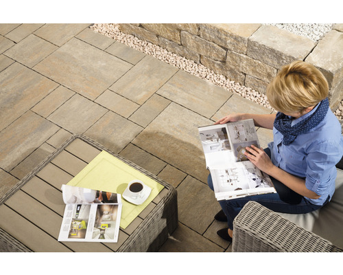 Terrasse mit Pflastersteinen, Natursteinmauer und lesender Frau