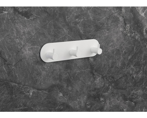 Weiße Wandgarderobe mit drei Haken an einer grauen Marmorwand.