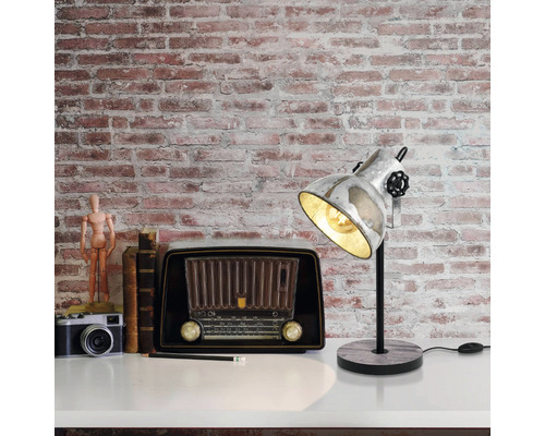 Dekorative Szene mit einer Schreibtischlampe, einem Radio, einer Kamera und Büchern auf einer weißen Oberfläche vor einer Ziegelwand.