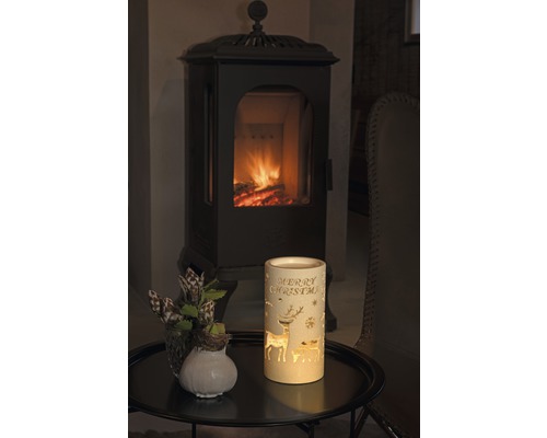 Dekorative Laterne mit dem Schriftzug Frohe Weihnachten, Reh Motiven und Kamin im Hintergrund.