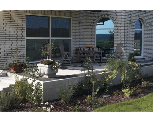 Terrasse mit Gartenmöbeln und bepflanzten Blumenkübeln vor einem Haus mit Backsteinfassade.