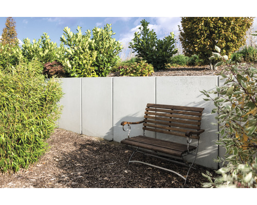 Gartenszene mit Betonmauer, bepflanzter Böschung und Holzbank