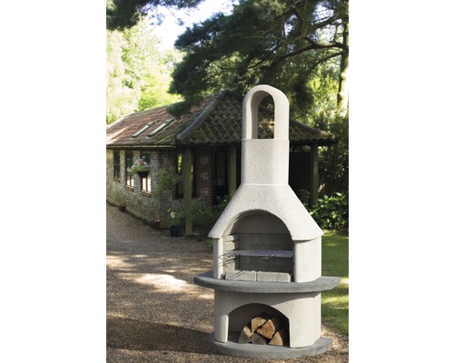 Außenaufnahme eines Steingrillofens mit Holzlager und Grillrost vor einem Gartenhaus