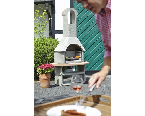 Gemauerter Grill mit Speisen im Garten und einer Person im Vordergrund