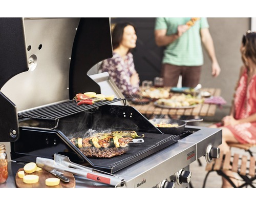 Edelstahl Grill mit Grillgut und Personen im Hintergrund