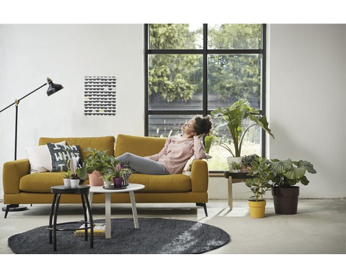 Wohnzimmer mit gelbem Sofa, Zimmerpflanzen und einer entspannten Person