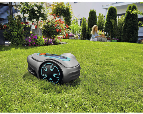Rasenmähroboter auf Rasenfläche im Garten mit Blumen und einer Frau