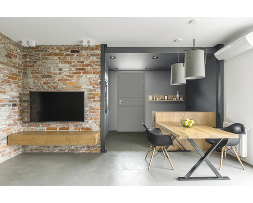 Wohnzimmer mit Ziegelwand, Fernseher, Holztisch und Stühlen.