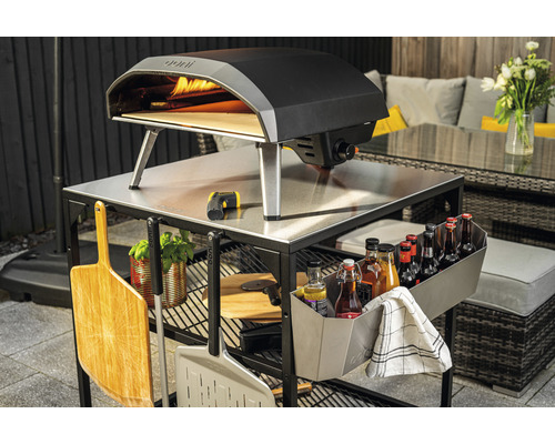 Ooni Pizzaofen auf einem Outdoorküchenwagen mit Zubehör im Garten.