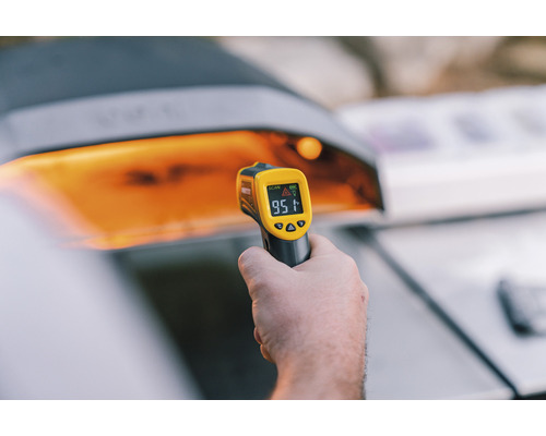 Hand hält ein Infrarot Thermometer vor einem Grill