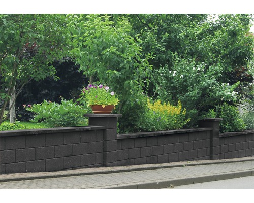 Eine Mauer aus Betonsteinen mit Pflanzen im Garten
