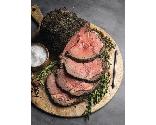 Gebratenes Rindfleisch mit Kräutern auf einem Holzbrett mit Salz und Thermometer.