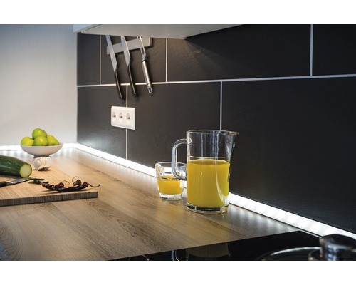 Küchenszene mit Saftkrug, Glas, Schneidebrett und Küchenutensilien vor schwarzem Fliesenspiegel