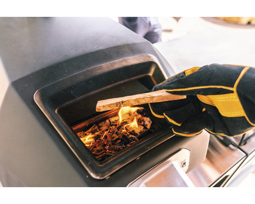 Befeuern eines Ofens mit Holz durch eine Person mit Handschuhen