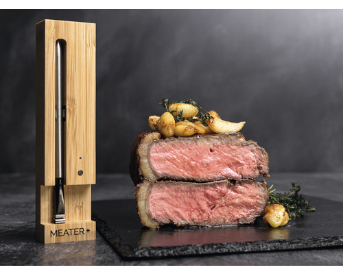 Fleischthermometer mit Ladevorrichtung aus Bambus neben Steak auf einem Teller