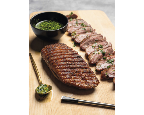 Gegrillte Entenbrust, tranchiert, mit Kräutersauce, Löffel und Pinsel auf Holzbrett