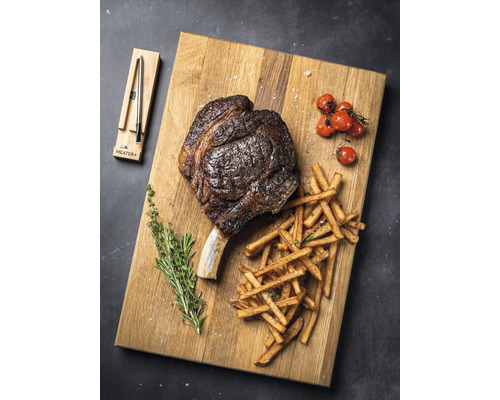 Tomahawk Steak mit Pommes Frites, Tomaten und Kräutern auf einem Holzbrett