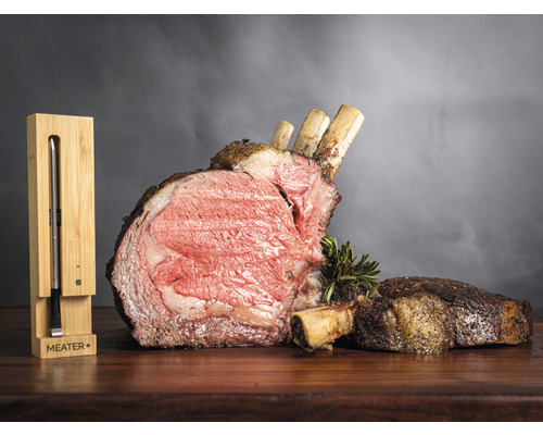 Gebratenes Rippenstück mit Knochen und einem Meater Plus Bratenthermometer auf einem Holztisch