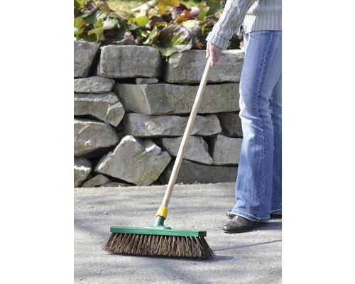 Eine Person kehrt mit einem Besen eine asphaltierte Fläche im Freien.