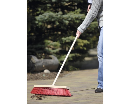 Eine Person kehrt mit einem Straßenbesen Laub auf Pflastersteinen.