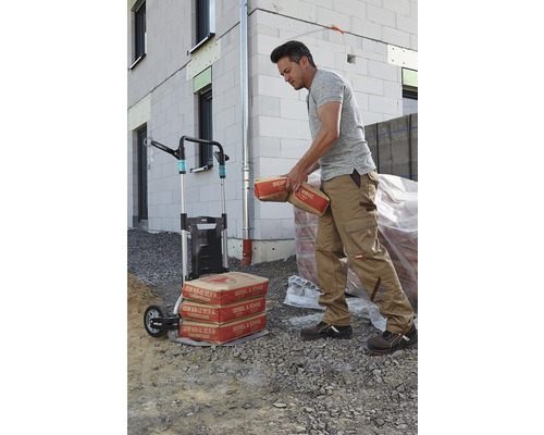 Mann transportiert Zementsäcke mit einer Sackkarre vor einem Haus