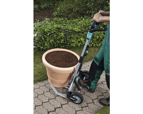 Eine Person transportiert einen Blumentopf mit einer Sackkarre im Garten.