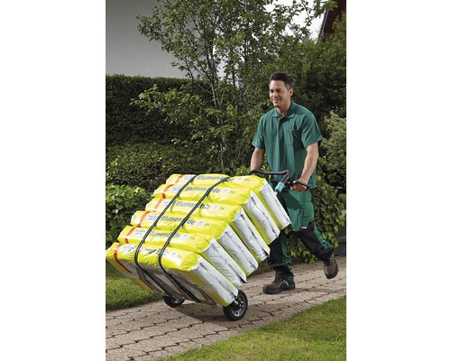 Eine Person schiebt mit einer Sackkarre Blumenerde durch einen Garten.