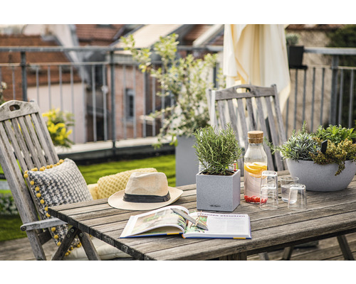 Balkonszene mit Holztisch, Stühlen, Pflanzen, Buch, Hut und Getränken für eine entspannte Atmosphäre