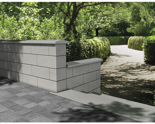 Gartenlandschaft mit Mauer aus Betonsteinen und gepflastertem Boden.