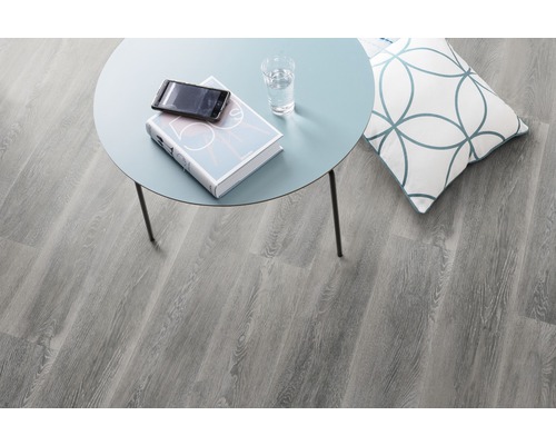 Dekorative Szene mit grauem Laminatboden, Beistelltisch, Kissen, Buch, Handy und Glas Wasser.