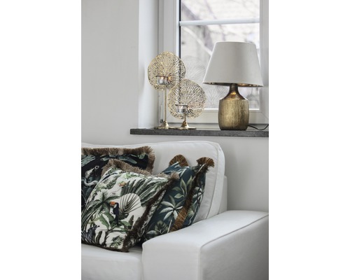 Dekoratives Wohnzimmer mit Sofa, Kissen mit Pflanzenmotiven, Tischleuchte und Windlichtern.