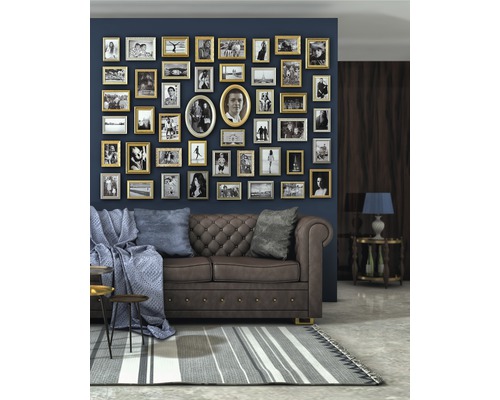 Wohnzimmer mit braunem Sofa, Kissen, Decke, Couchtisch und einer Wand voller Bilderrahmen