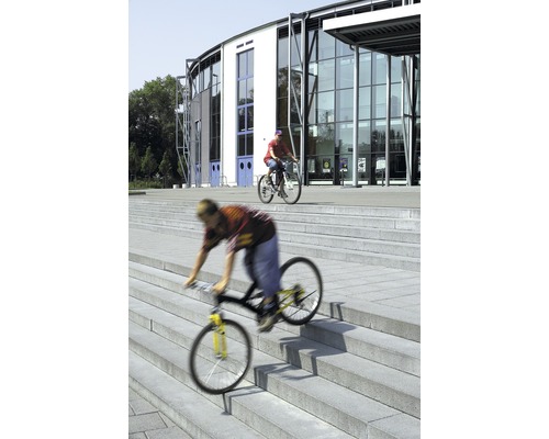 Zwei Personen fahren mit Fahrrädern vor einem Gebäude Treppen hinunter.
