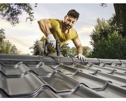 Ein Mann befestigt Metalldachziegel mit einem Akkuschrauber auf einem Dach.