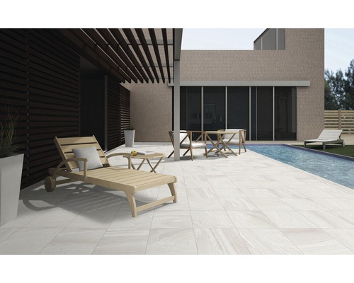 Terrasse mit Fliesen, Liegestuhl, Tisch und Stühlen neben einem Pool.