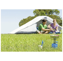Szene mit Gaskocher, Campinggeschirr und Zelt im Freien auf einer Wiese.