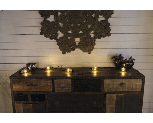 Kommode mit Schubladen, Dekoration und Lichterkette vor einer Holzwand