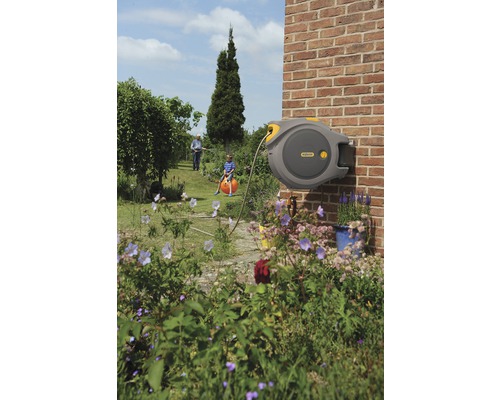 Automatische Schlauchbox an einer Backsteinmauer in einem Garten mit spielendem Kind