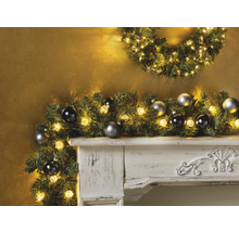 Dekorativer Kamin mit Weihnachtsgirlande, Lichtern und Christbaumkugeln.