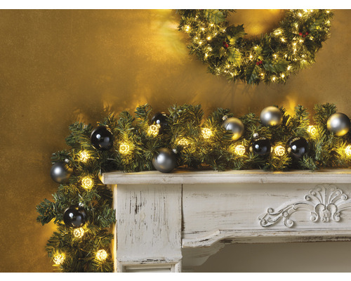 Dekorativer Kamin mit Weihnachtsgirlande, Lichtern und Christbaumkugeln.